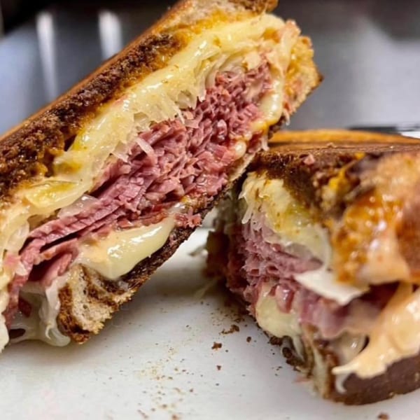 Close-up of a grilled sandwich, cut in half, revealing layers of pastrami, melted cheese, and sauerkraut.
