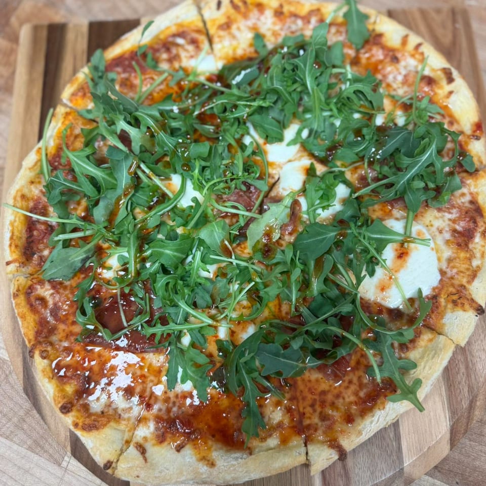 A freshly baked pizza from Seneca's Italian Deli & Market, topped with arugula and balsamic glaze.